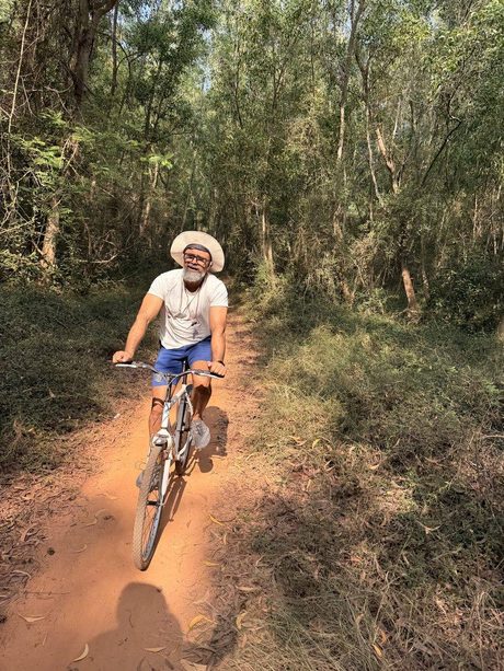 Venky riding a mountain bike alone along a red dirt trail through forest.